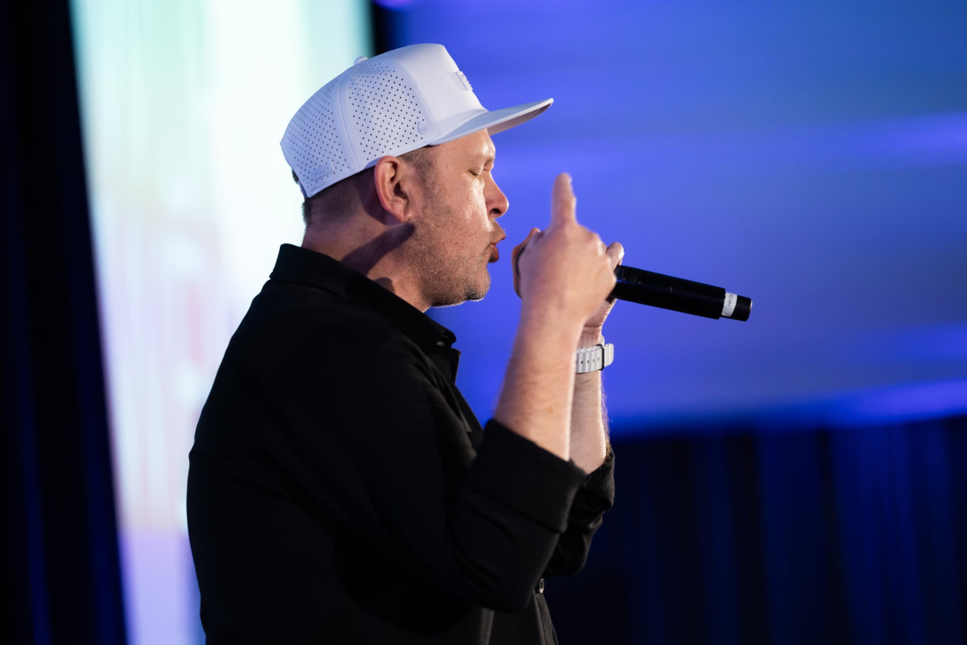 Close-up of Michael King Jr. performing with a microphone against a blue backdrop